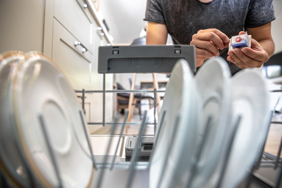 	mężczyzna wkładający tabletkę do zmywarki